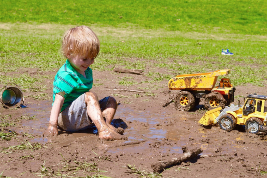 A boy playing with trucks in the mud.