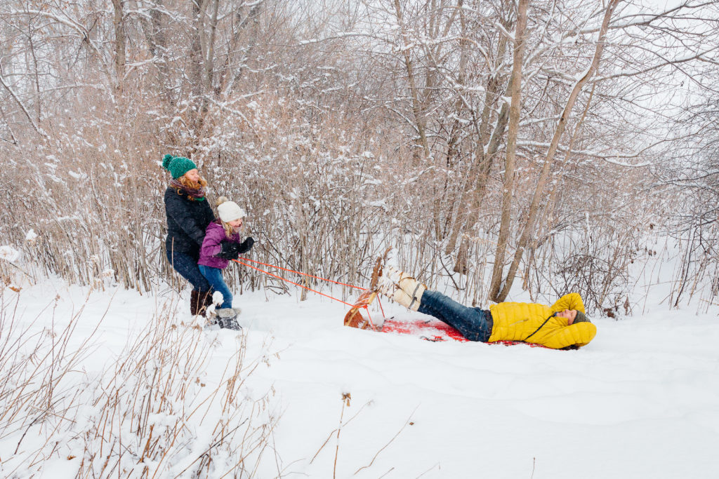 A mother and daughter pull the father on a tobbogan.