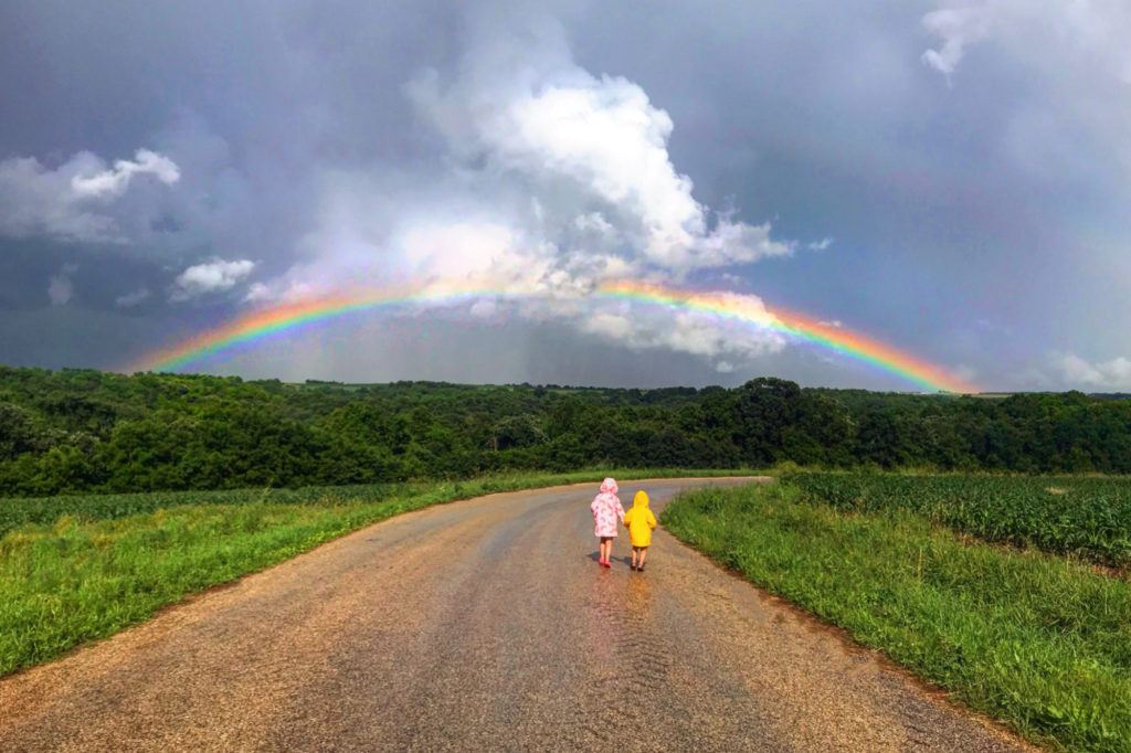 Two children walk toward a rainbow.