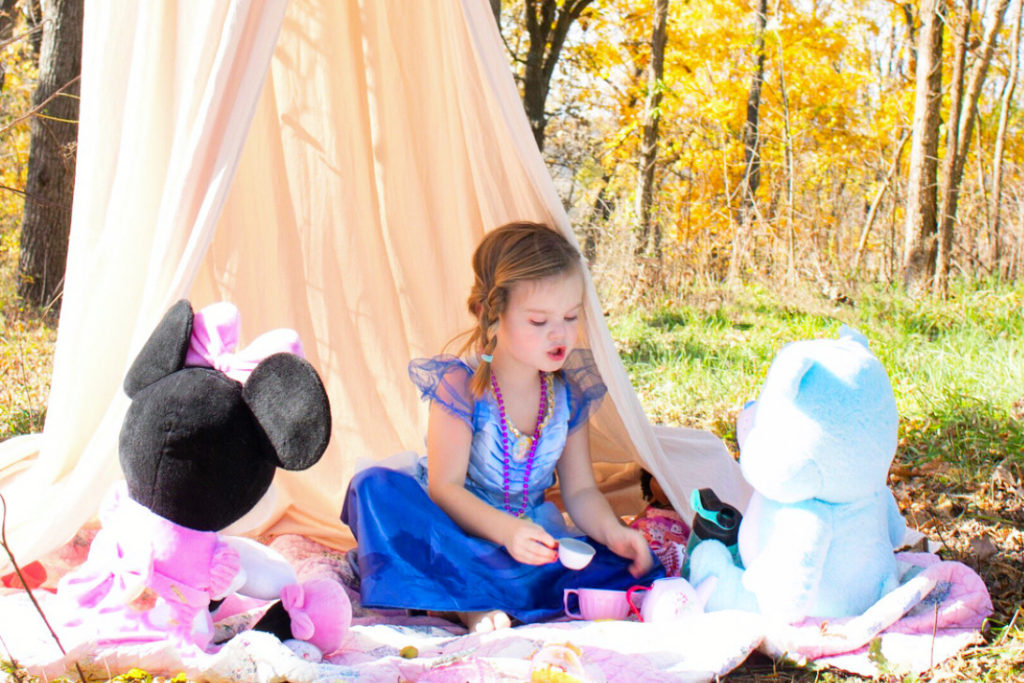 A girl has a tea party with stuffed animals in the woods.