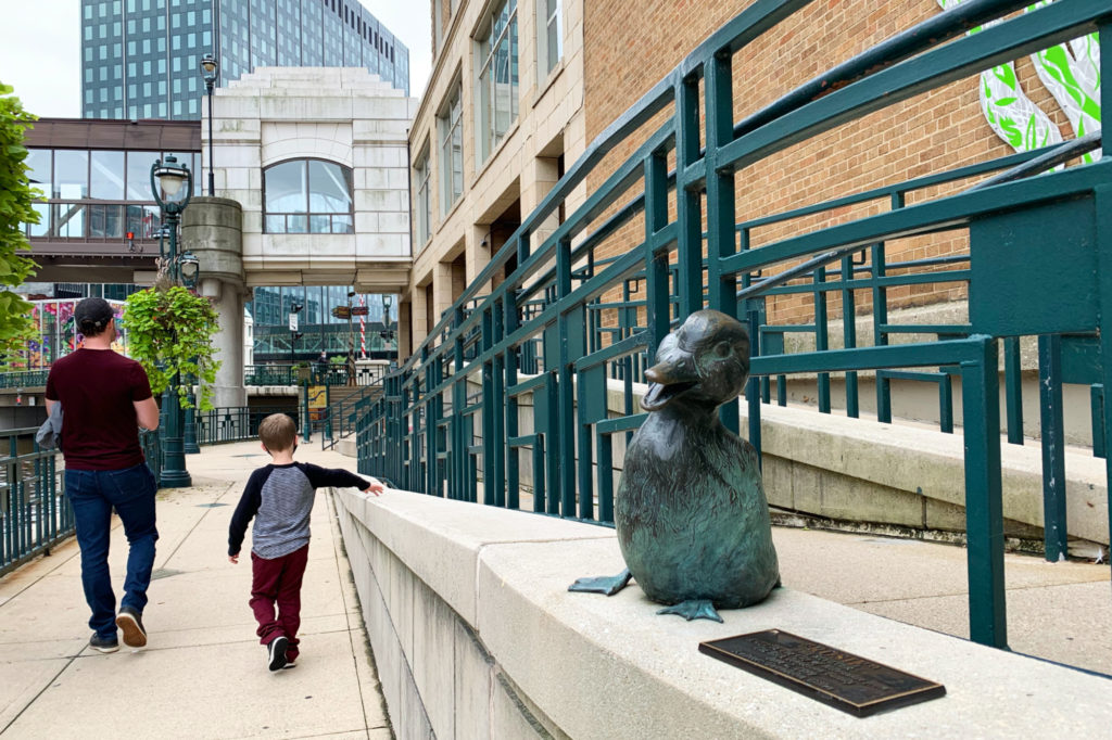 A father and son walk past a duck sculpture on the Riverwalk in Milwaukee.