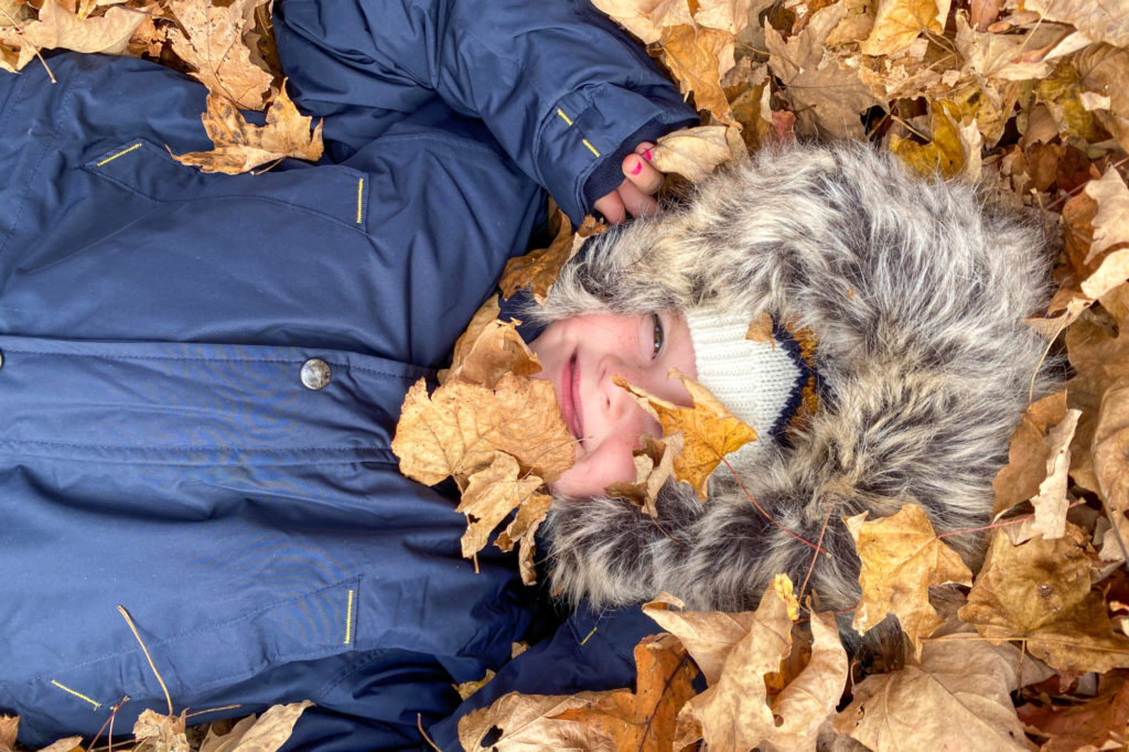 A girl lies in a pile of fall leaves.