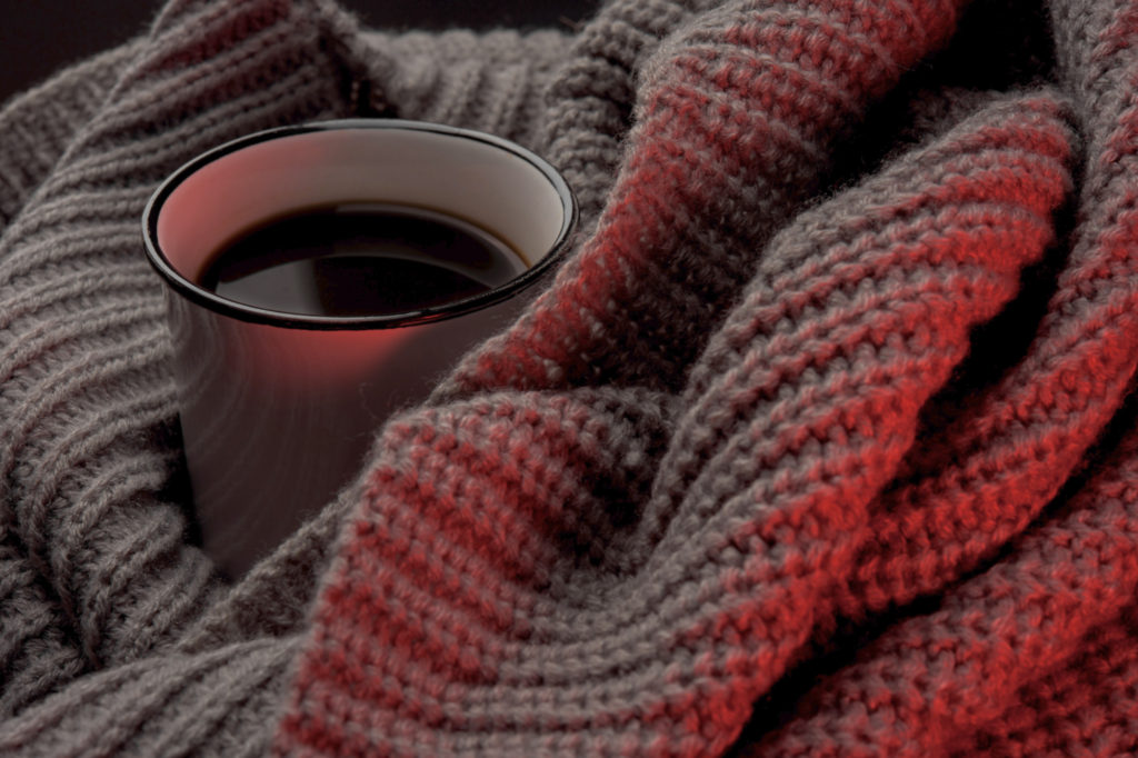 A cup of coffee nestled into a knit blanket.