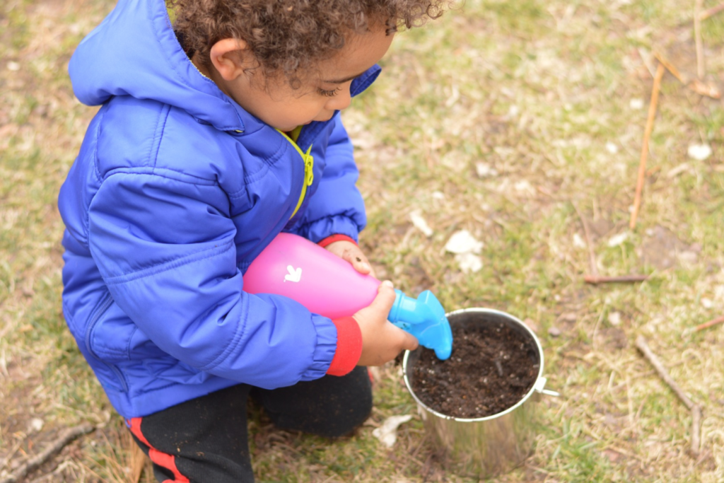 A child waters seeds in a bucket of dirt.