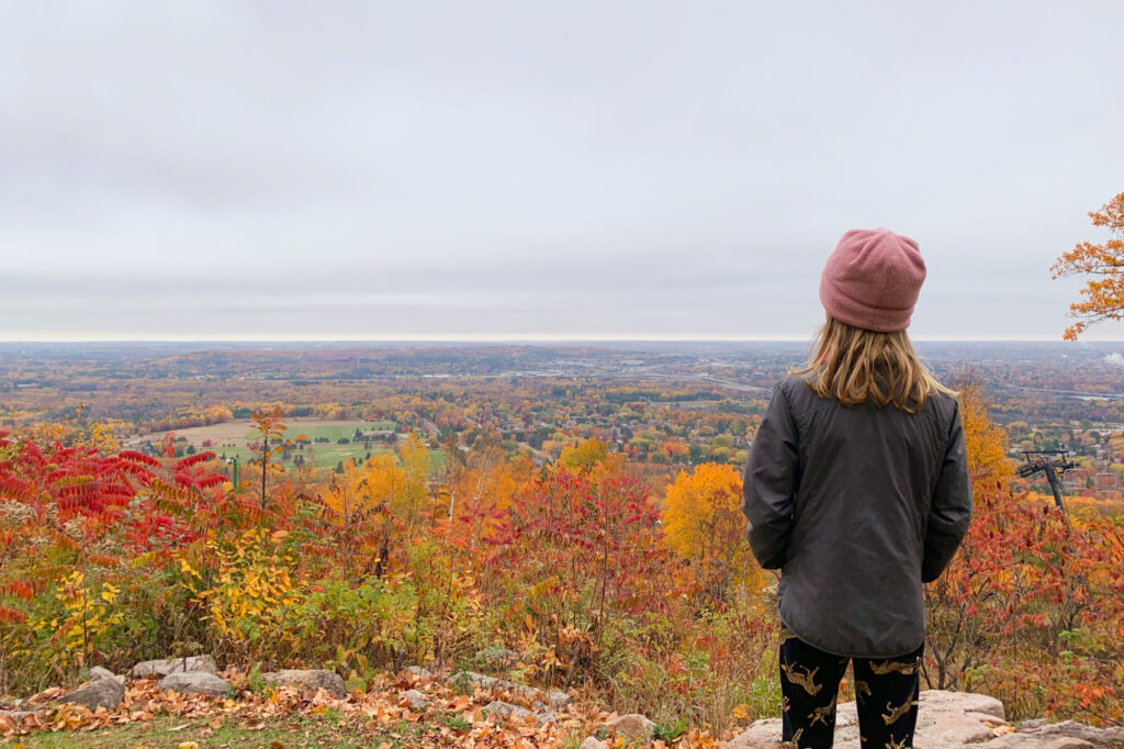 A girl stands overlooking the colorful trees and vista on a fall visit to Rib Mountain State Park.