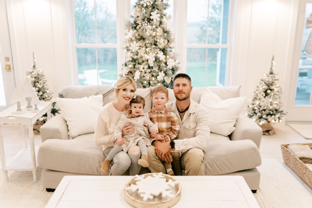 Ashley Kix and her husband and two kids sit on a sofa in front of their Christmas tree.