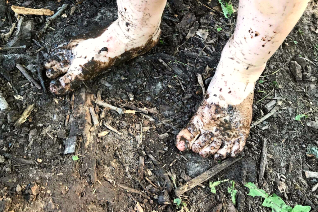 A child's bare feet get muddy while standing in the dirt.