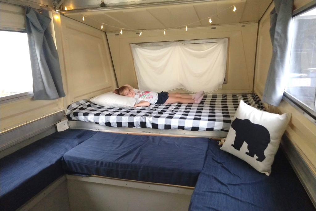 A girl lies on a bed inside her family's pop-up camper. 