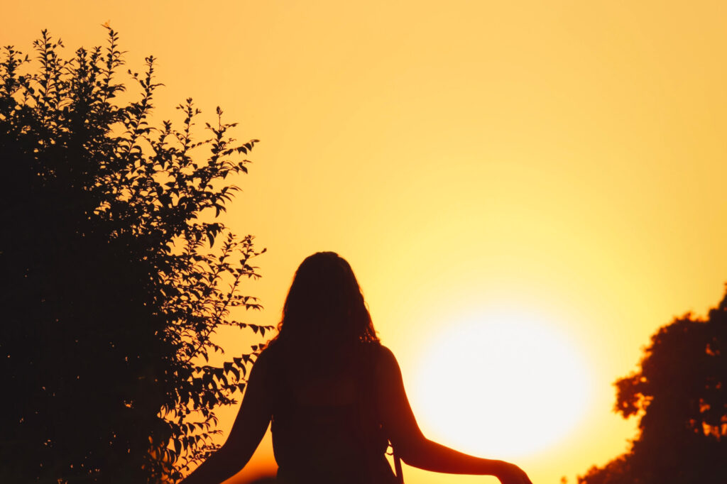 A woman stands by a sun-filled sky.