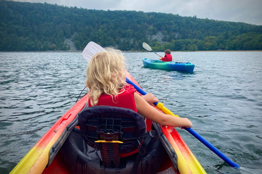 A girl paddles from the front of a canoe while a boy paddles in another nearby.