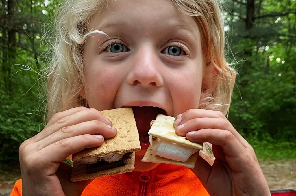 A girl bites into two s'mores.